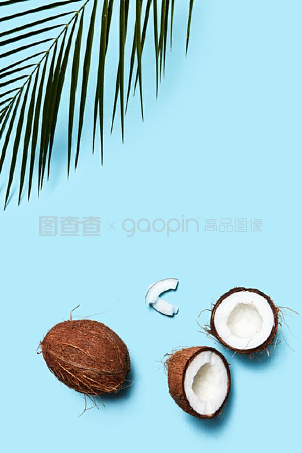 一片椰子和整個椰子,在藍色背景上有一片棕櫚綠葉。食物成分。平鋪。一個由有機的一半和一個椰子組成的美麗組成的藍色背景裝飾著一塊飾板,上面有一片平鋪。